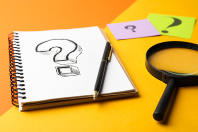 Photo of Notebook with question mark, pen and magnifier glass on color background, closeup
