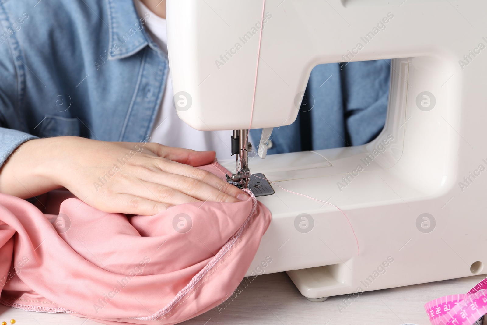 Photo of Seamstress working with sewing machine at white table indoors, closeup