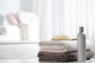 Photo of Towels with hair brush and shampoo on table. Space for text