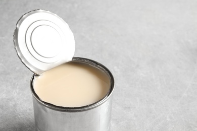 Photo of Tin can with condensed milk on grey background, space for text. Dairy product