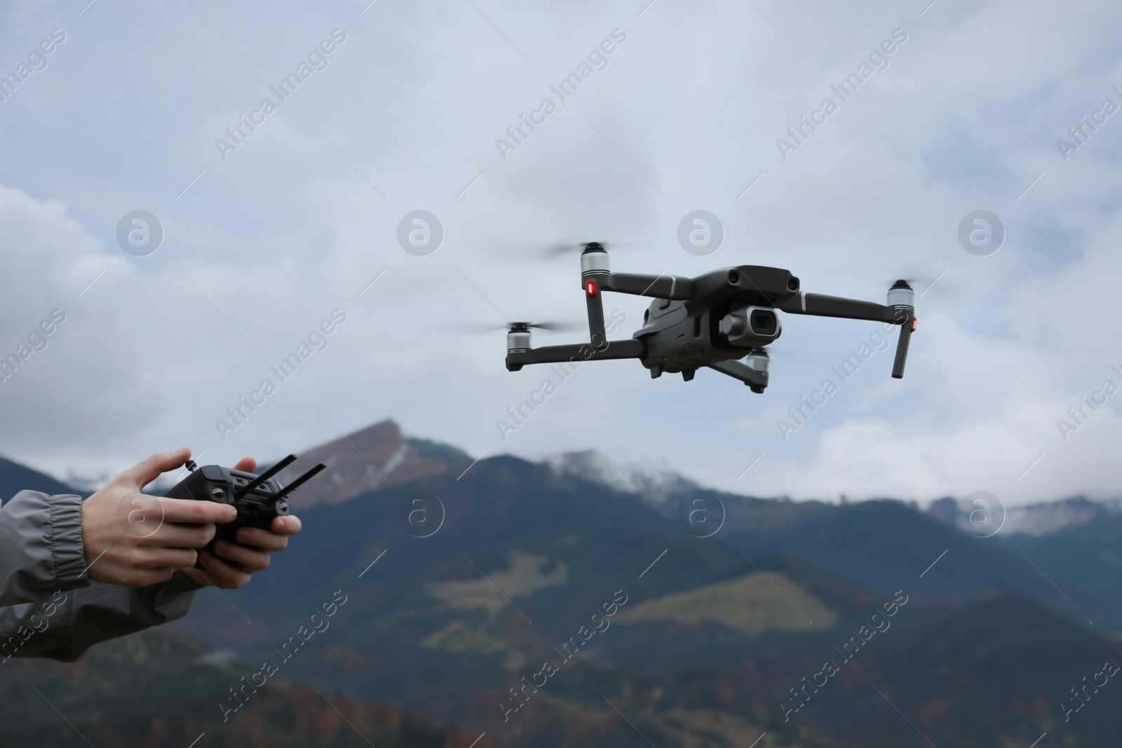 Photo of Woman operating modern drone with remote control in mountains, closeup