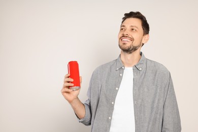 Photo of Happy man holding red tin can with beverage on light grey background. Space for text