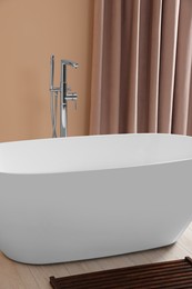 Stylish bathroom interior with ceramic tub near beige curtains