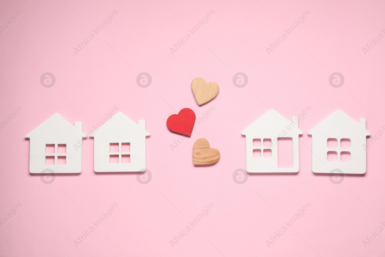 Photo of Long-distance relationship concept. Decorative hearts between white house models on pink background, flat lay