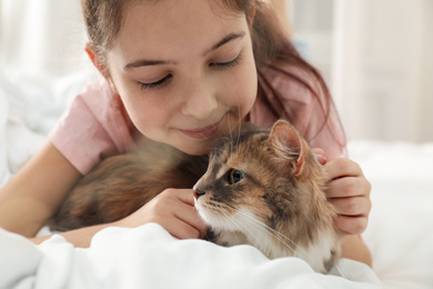 Cute little girl with cat lying on bed at home, closeup. First pet