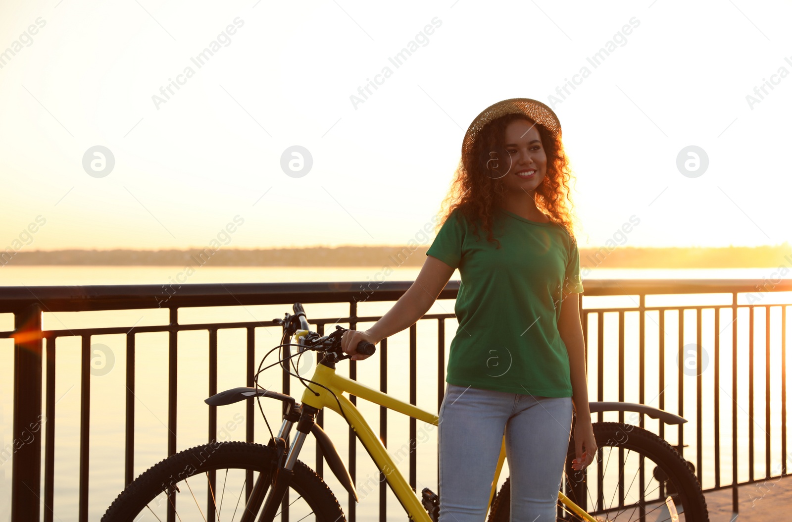 Photo of Beautiful young African-American woman with bicycle on city waterfront at sunset