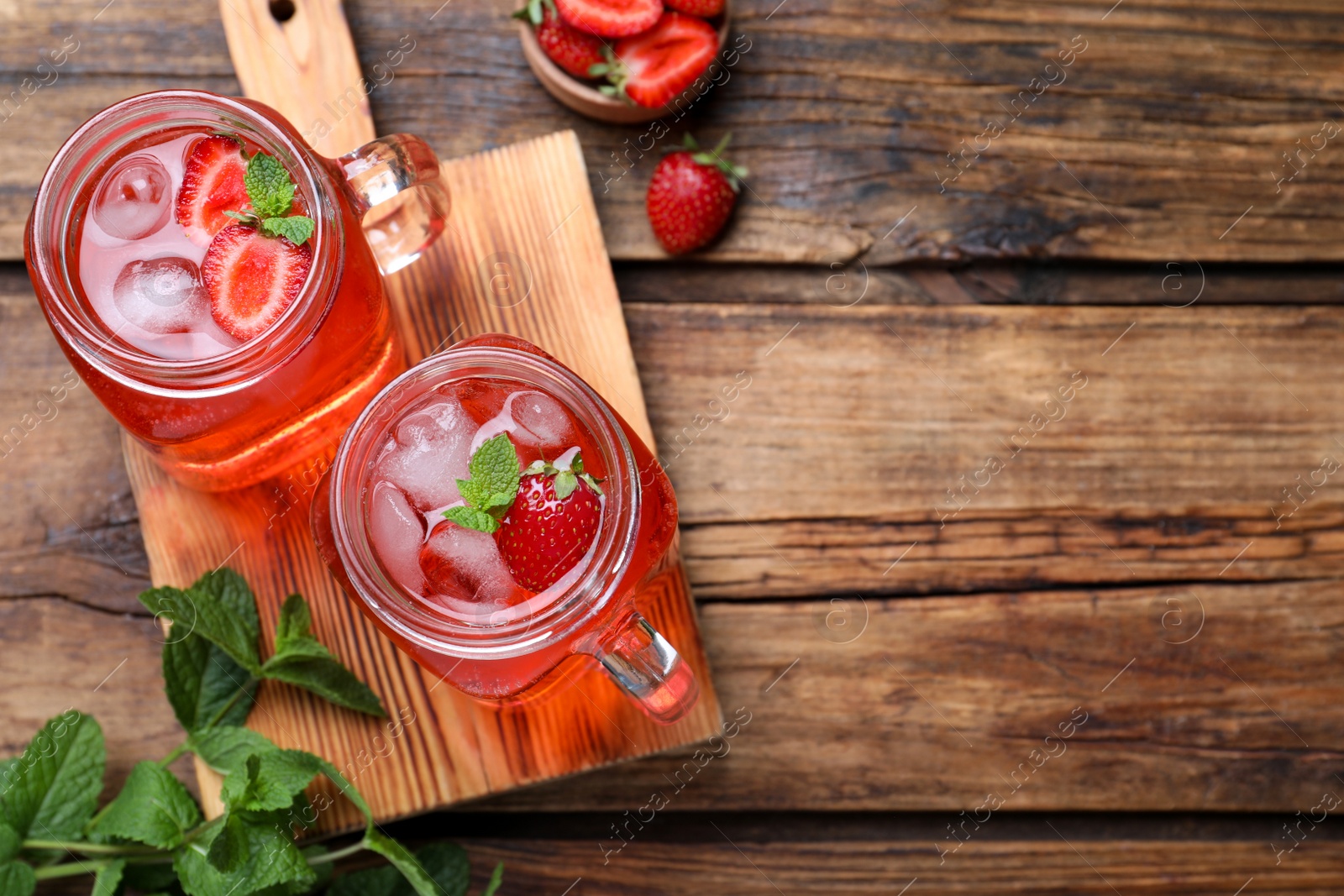 Photo of Delicious strawberry lemonade made with soda water and fresh ingredients on wooden table, flat lay. Space for text