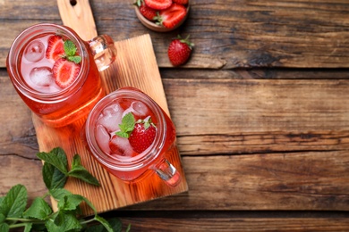 Photo of Delicious strawberry lemonade made with soda water and fresh ingredients on wooden table, flat lay. Space for text