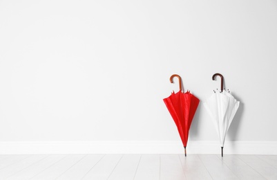 Photo of Beautiful bright umbrellas on floor near white wall with space for design