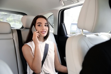 Photo of Young businesswoman talking on mobile phone in luxury car with driver. Chauffeur service