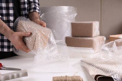 Photo of Man covering box with bubble wrap at table in warehouse, closeup