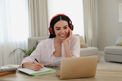 Photo of Young woman taking notes during online webinar at table indoors