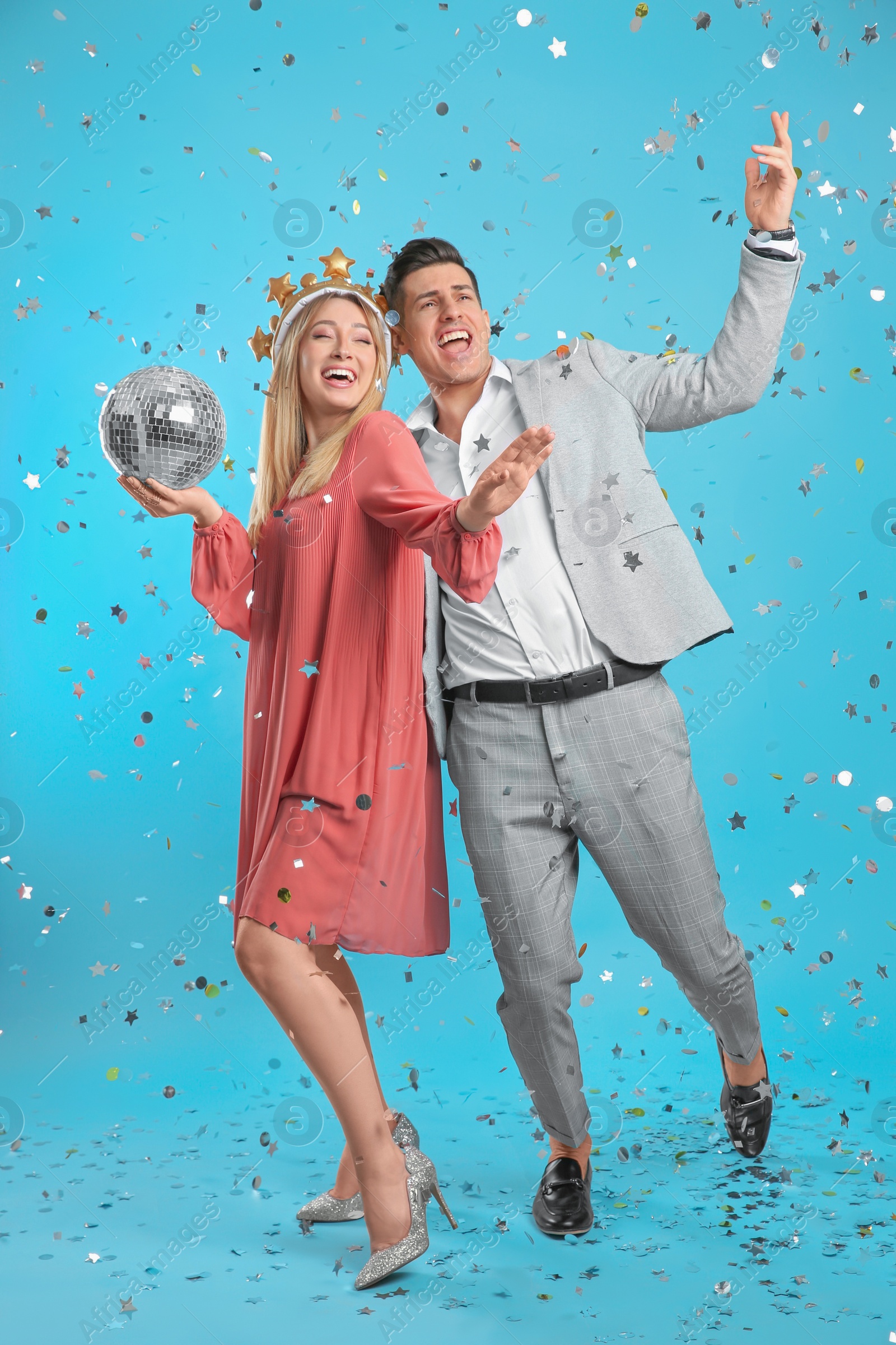 Photo of Happy couple with disco ball and confetti on light blue background