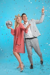 Photo of Happy couple with disco ball and confetti on light blue background