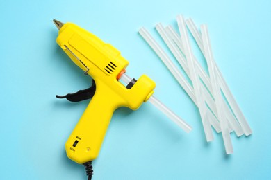 Yellow glue gun and sticks on turquoise background, flat lay