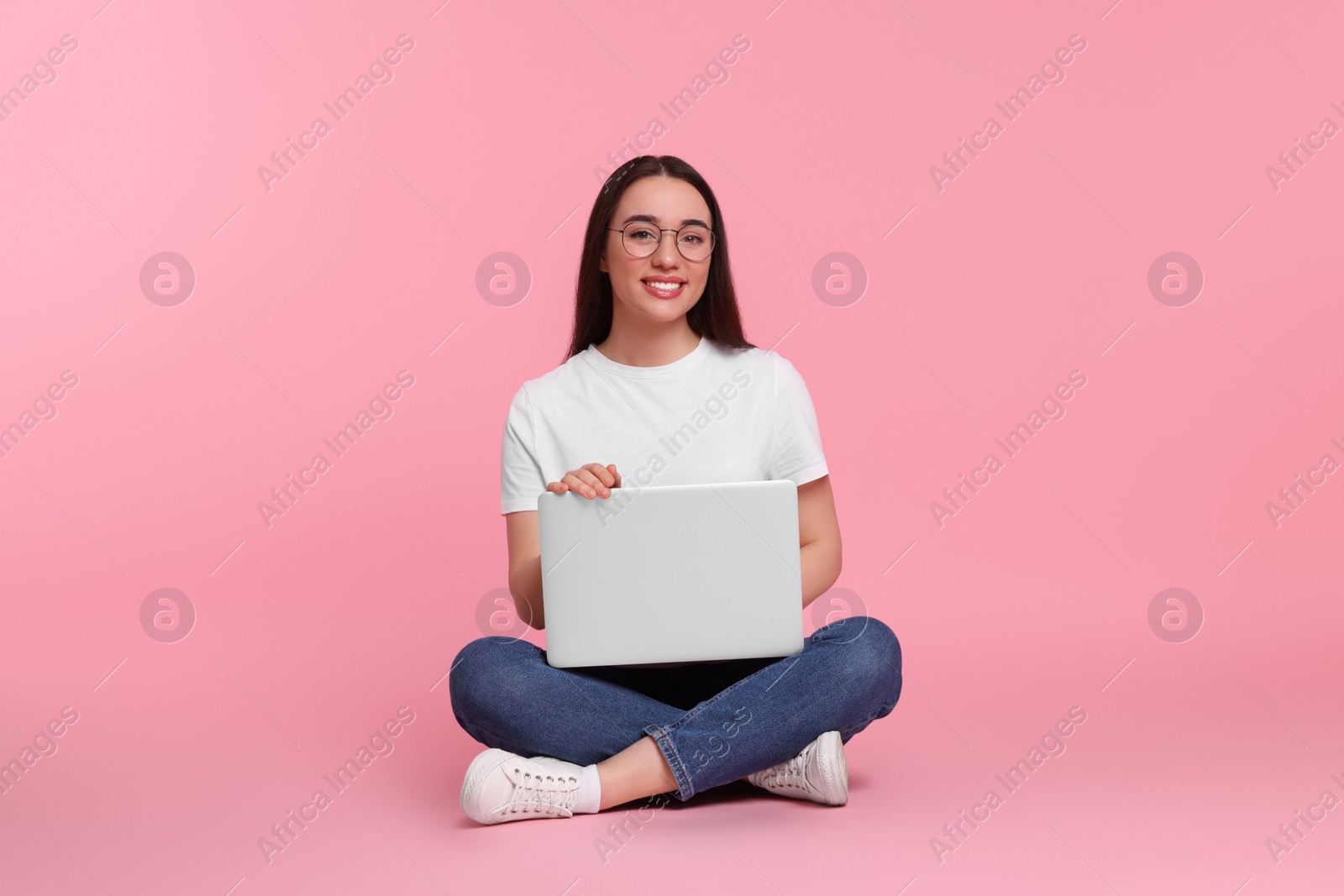 Photo of Smiling young woman with laptop on pink background