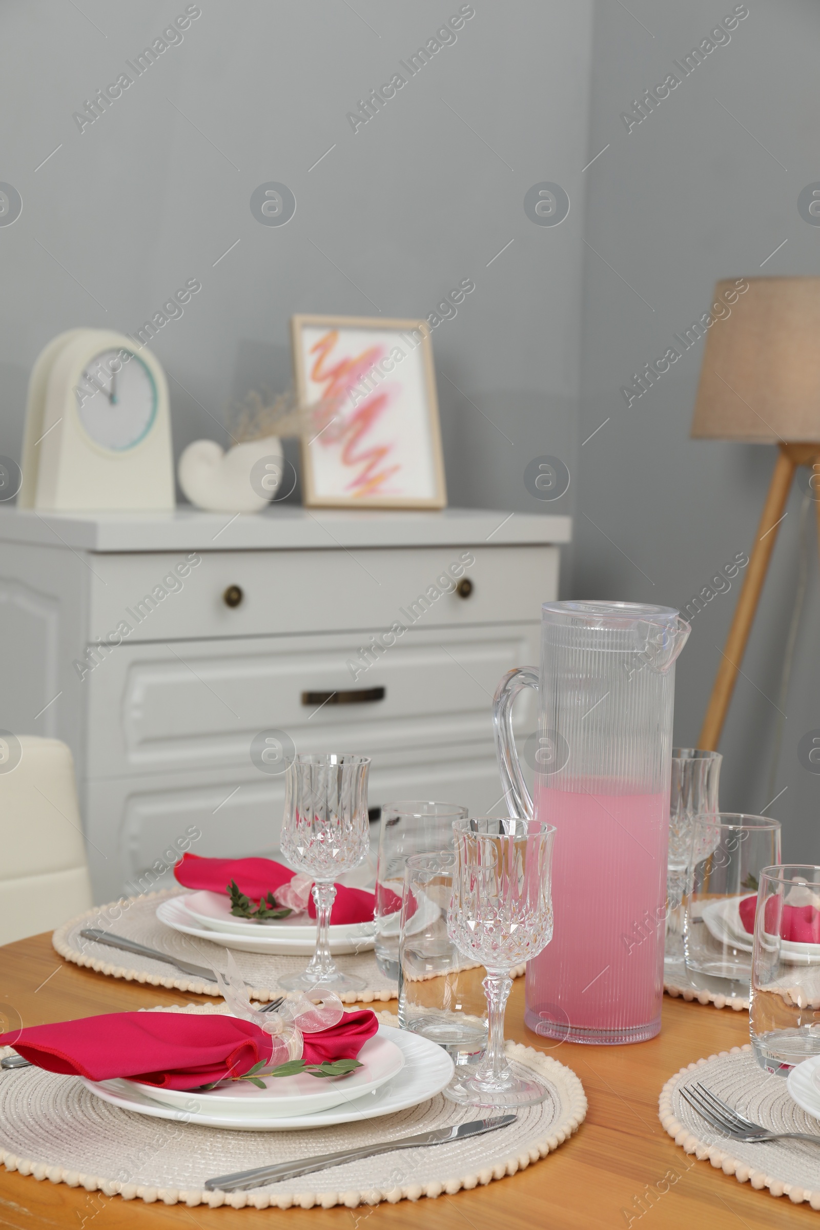 Photo of Color accent table setting. Glasses, plates, jug of beverage and pink napkins in dining room