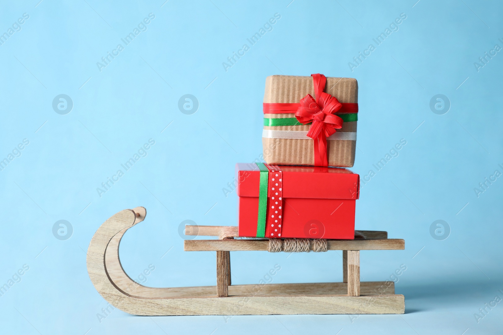 Photo of Wooden sleigh with Christmas gift boxes on light blue background