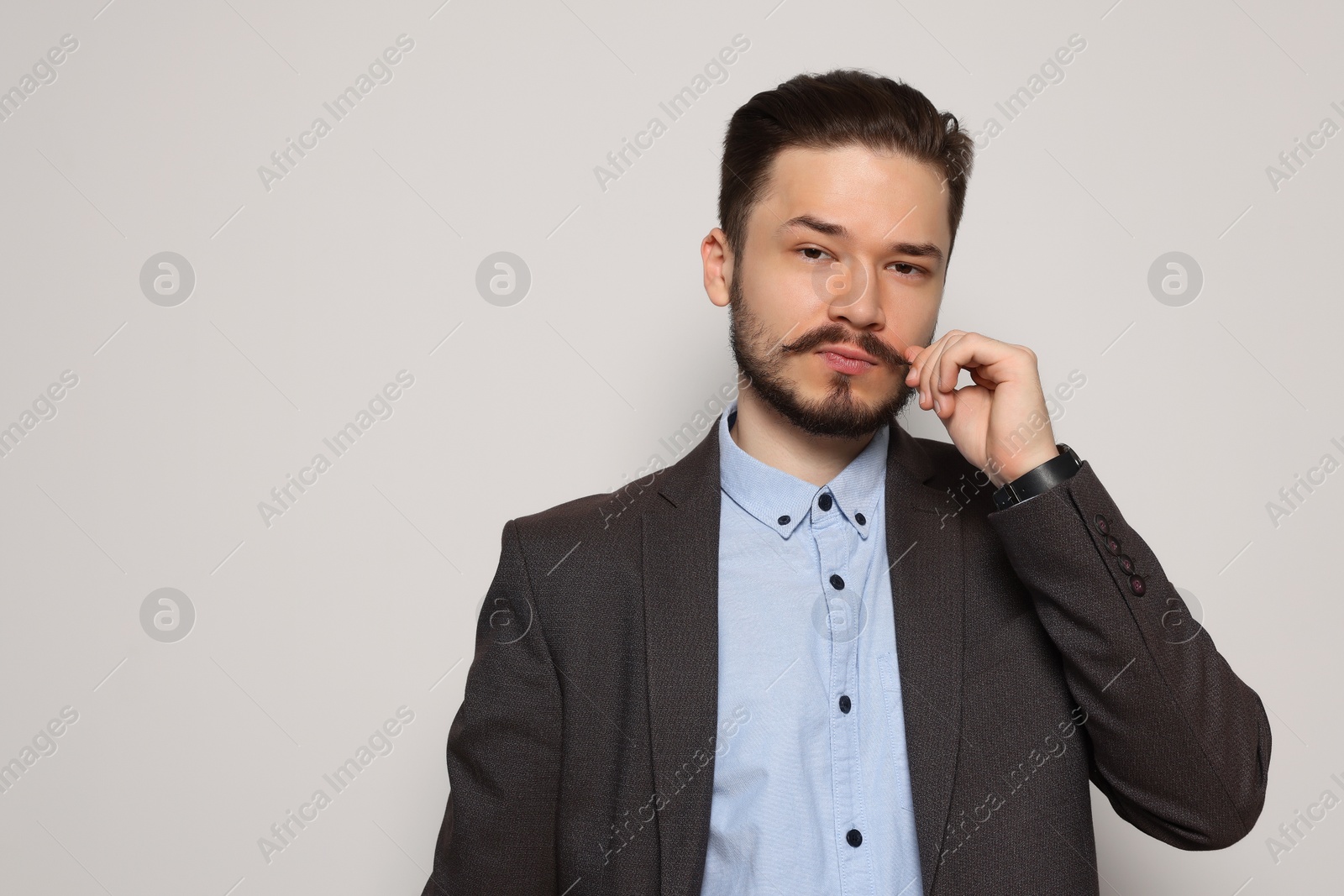 Photo of Handsome man in suit touching mustache on light grey background. Space for text