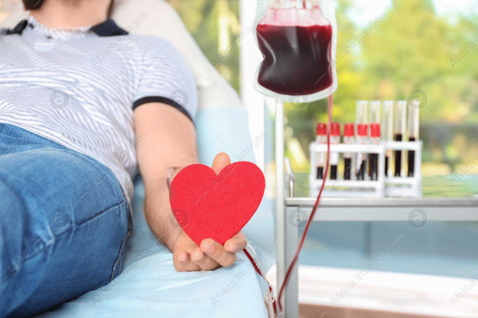 Photo of Man holding heart while making blood donation at hospital, closeup