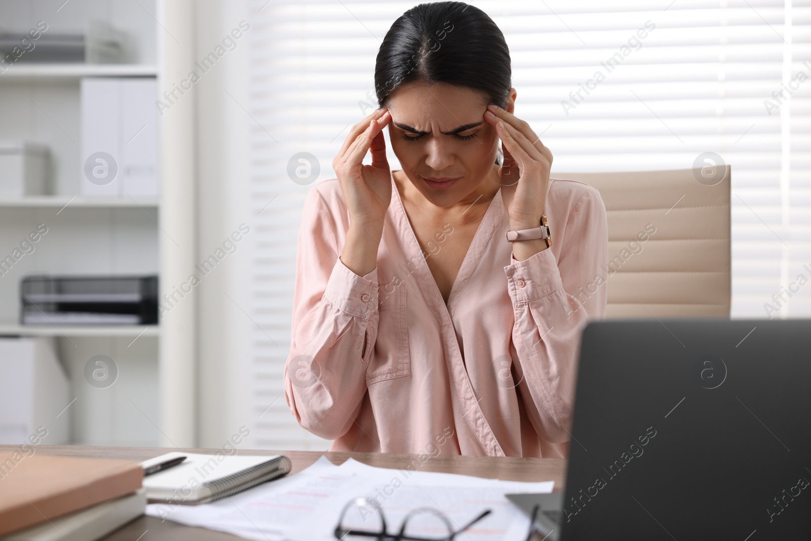 Photo of Young woman suffering from headache at wooden table in office