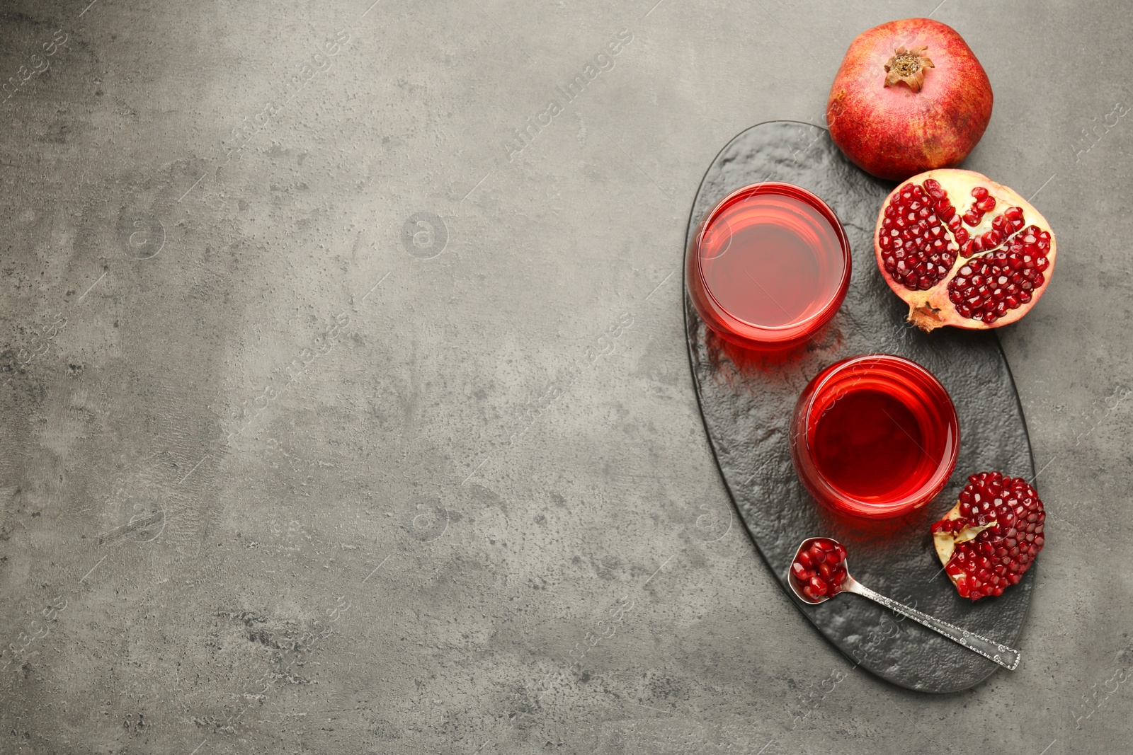 Photo of Tasty pomegranate juice in glasses and fresh fruit on grey table, top view. Space for text