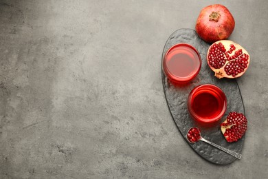 Photo of Tasty pomegranate juice in glasses and fresh fruit on grey table, top view. Space for text