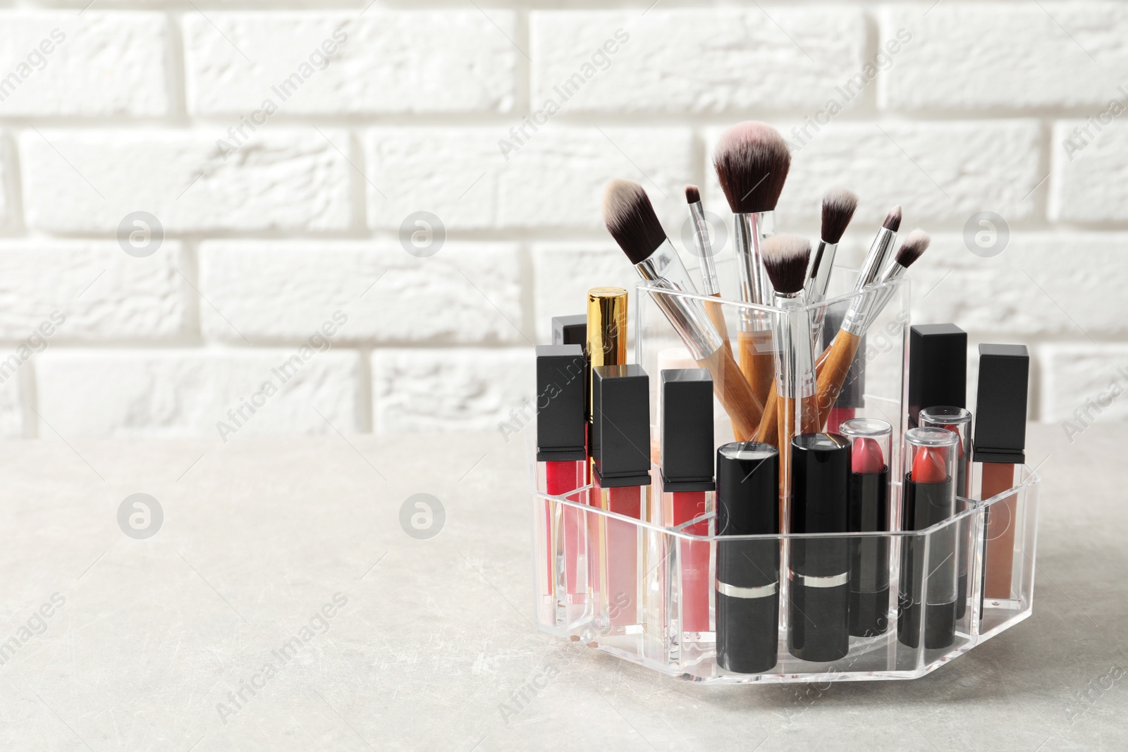 Photo of Lipstick holder with different makeup products on table against brick wall. Space for text