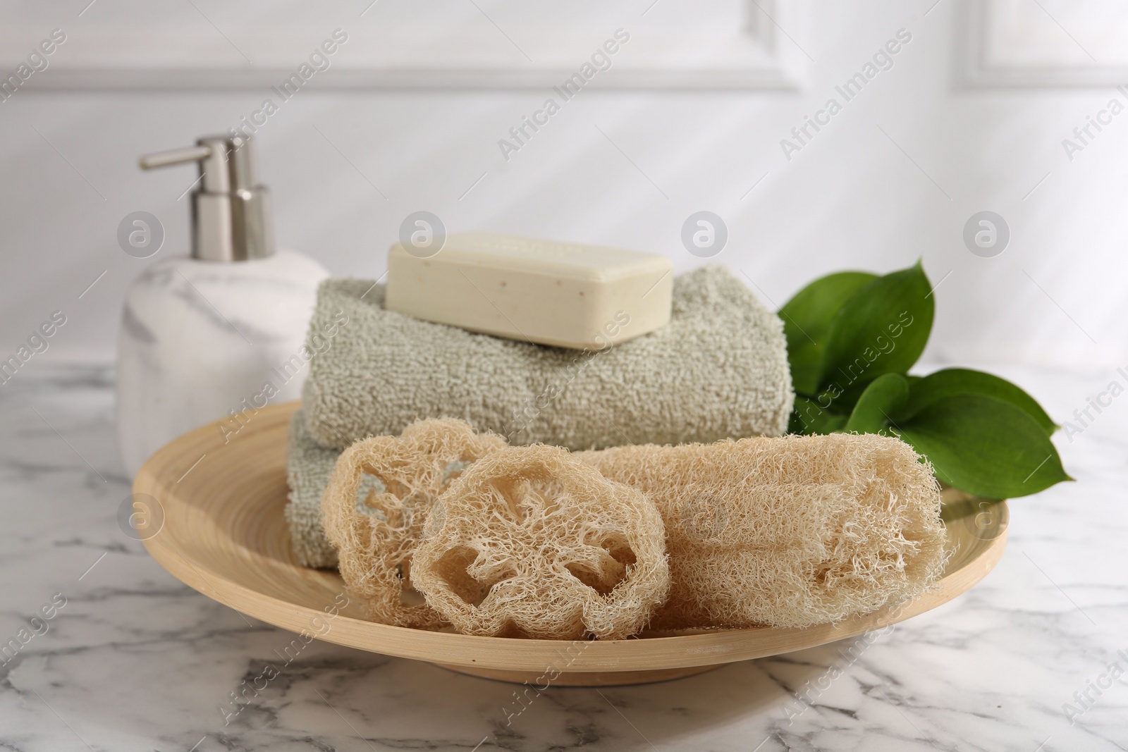 Photo of Loofah sponges, soap, towels and green leaves on white marble table