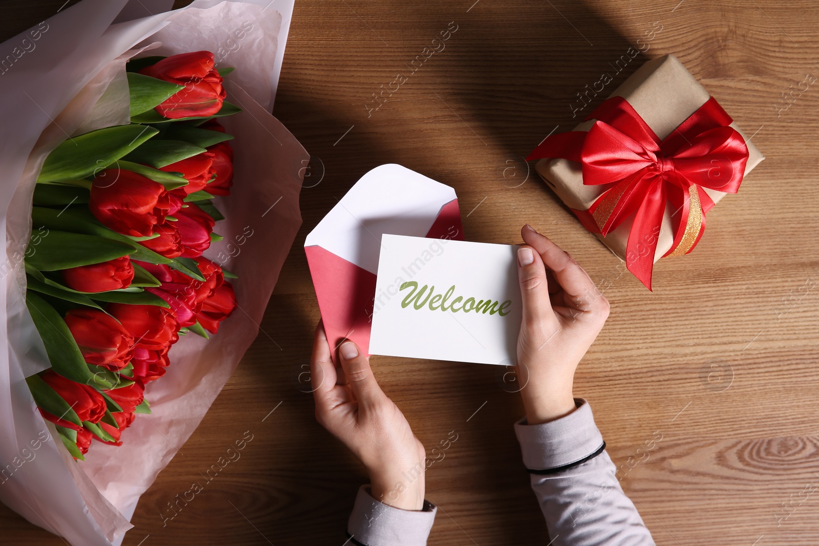 Image of Woman holding envelope and Welcome card at table with bouquet and gift box, top view