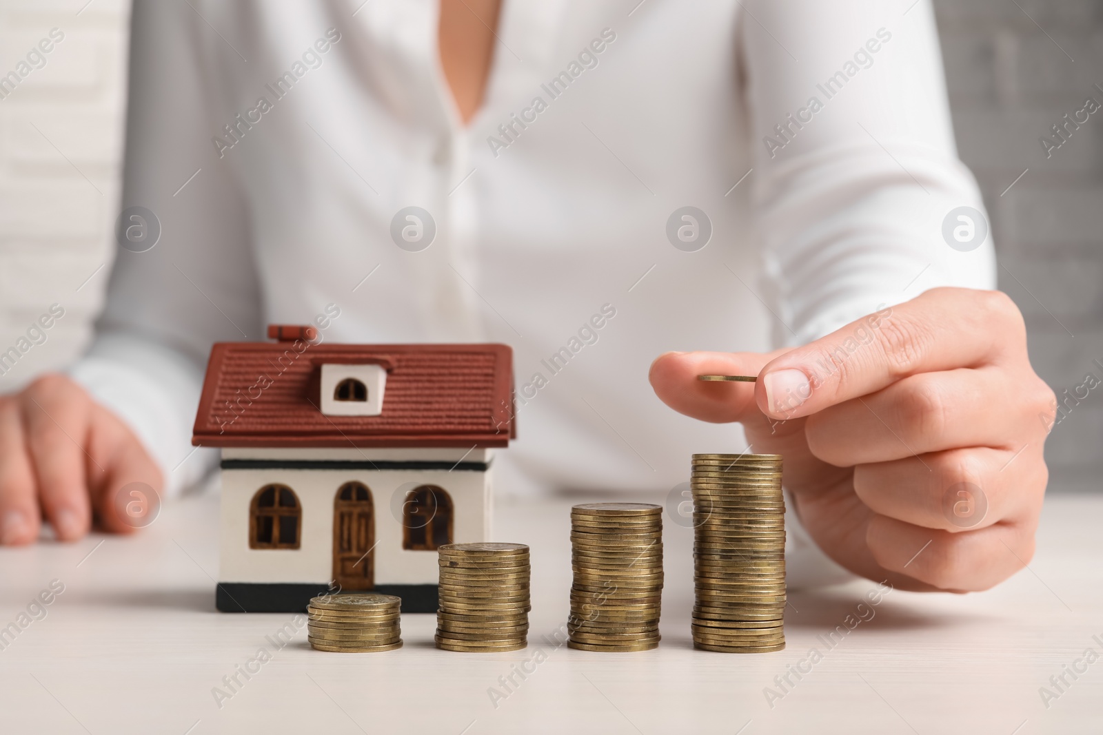 Photo of Woman stacking coins near house model at light table, closeup