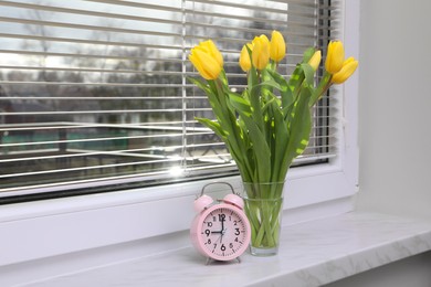 Photo of Wonderful tulips and alarm clock on window sill indoors, space for text. Spring atmosphere