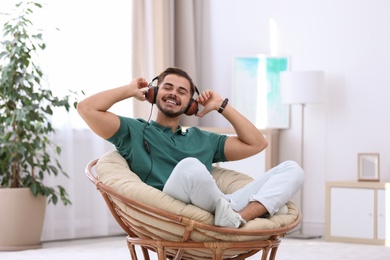 Handsome young man listening music in armchair at home