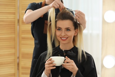 Photo of Hair styling. Professional hairdresser working with woman while she drinking coffee in salon, closeup