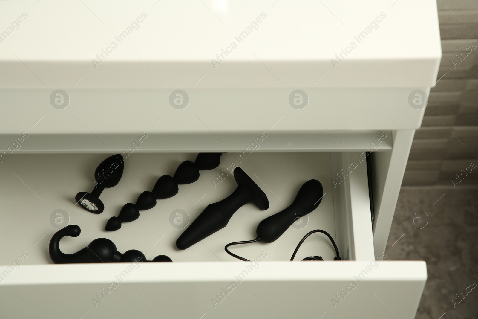 Photo of Black vibrator, anal plugs and beads in drawer indoors. Sex toys