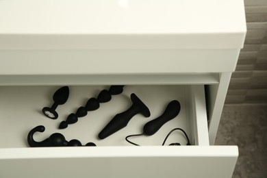 Photo of Black vibrator, anal plugs and beads in drawer indoors. Sex toys