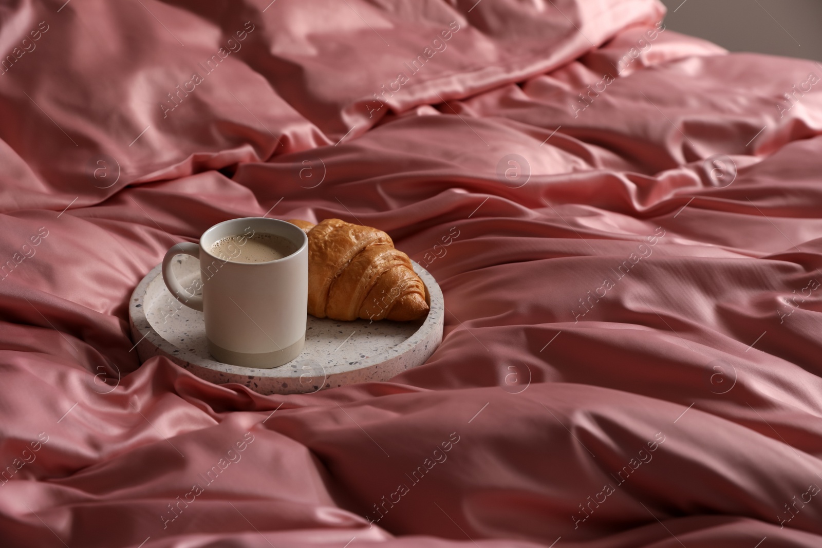 Photo of Tray with tasty croissant and cup of coffee on beautiful pink silk linens