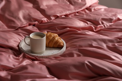 Photo of Tray with tasty croissant and cup of coffee on beautiful pink silk linens