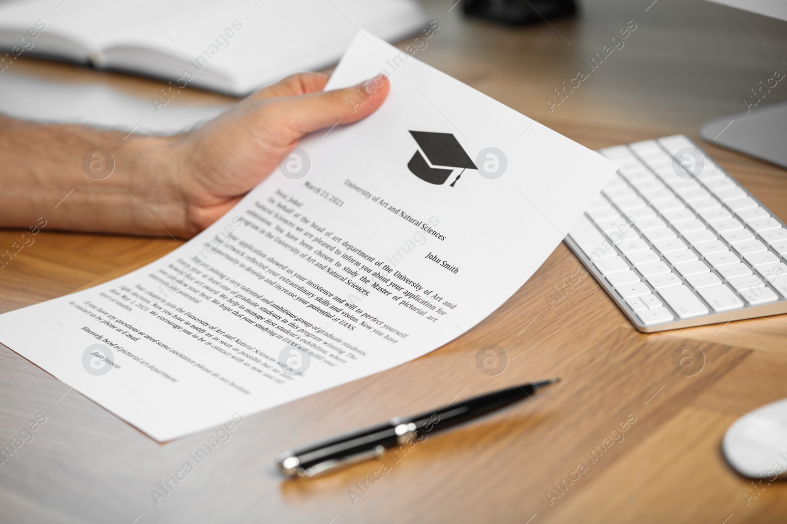 Photo of Student with acceptance letter from university at wooden table indoors, closeup