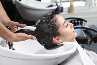 Stylist washing client's hair at sink in beauty salon