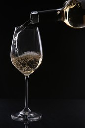 Photo of Pouring white wine from bottle into glass on black background
