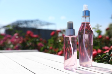 Bottles of facial toner with essential oil and blurred rose bushes on background. Space for text