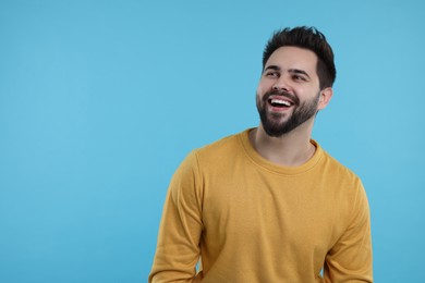 Photo of Handsome young man laughing on light blue background, space for text