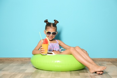 Photo of Cute little girl with inflatable ring and glass of cocktail near color wall