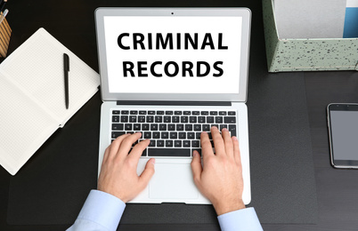 Image of Man using laptop with words CRIMINAL RECORDS at table, top view