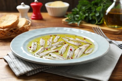 Photo of Tasty pickled anchovies with spices on wooden table, closeup