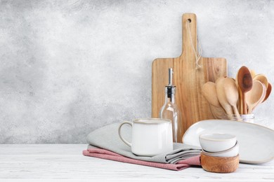 Different kitchenware and dishware on white wooden table against textured wall. Space for text