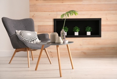 Photo of Living room interior with vases on table and armchair near wooden wall. Space for text