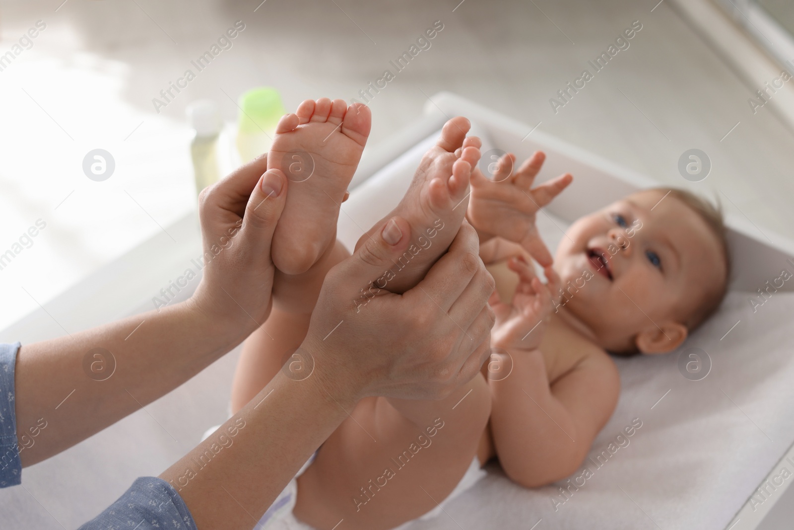 Photo of Mother massaging her baby with oil on changing table at home, closeup