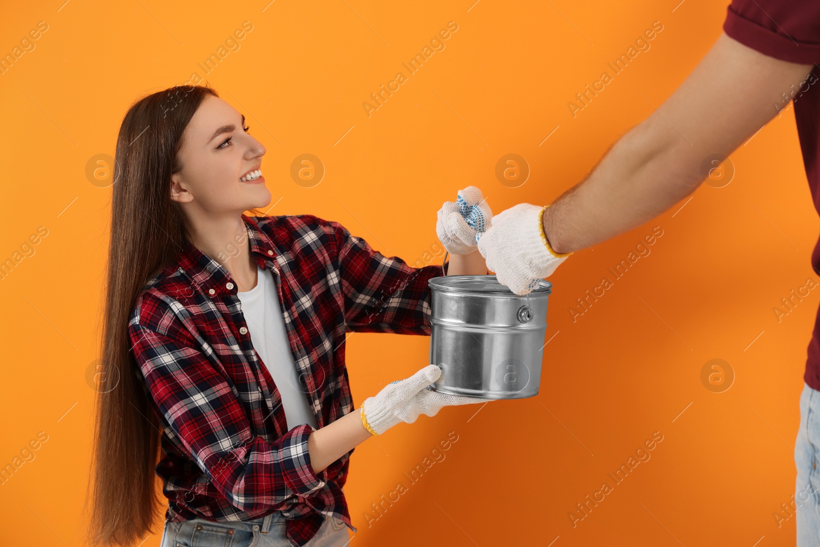 Photo of Woman giving man can of paint near orange wall. Interior design